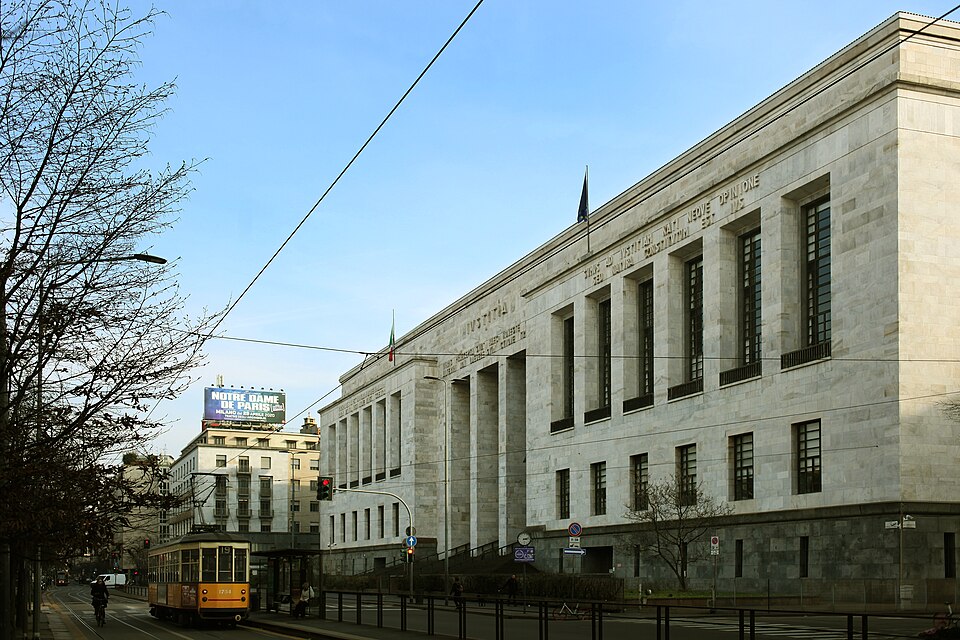 大理石の柱が並ぶミラノ裁判所の建物と、前を走るオレンジ色のトラム